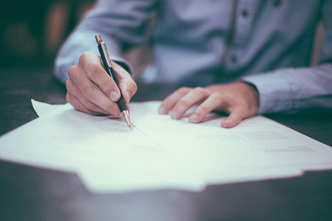 Close-up of a person reviewing and signing business documents.