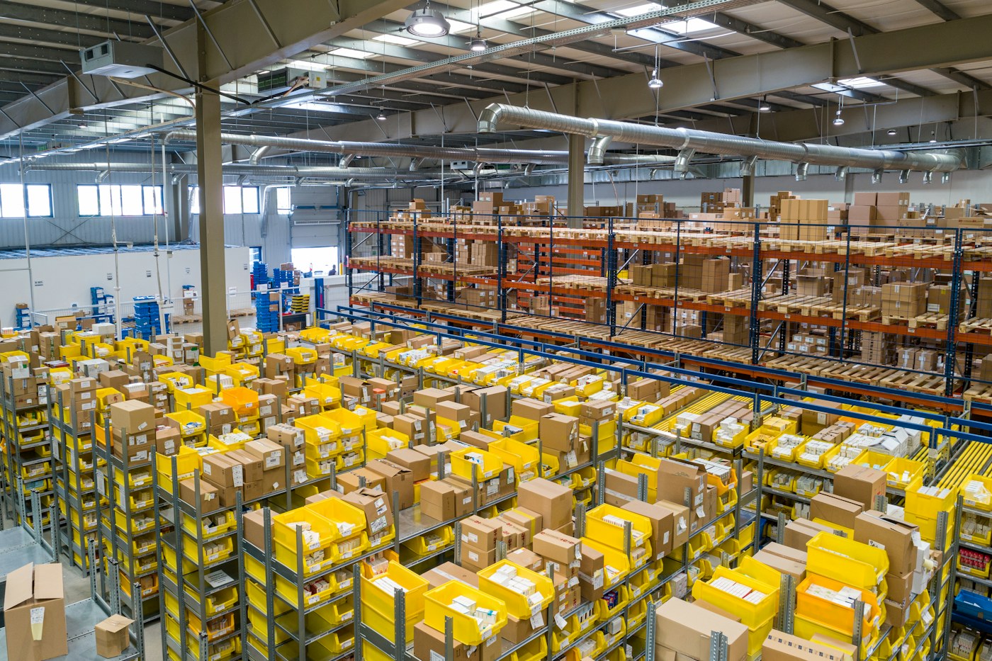 Organized warehouse shelves holding cartons and yellow picking bins.